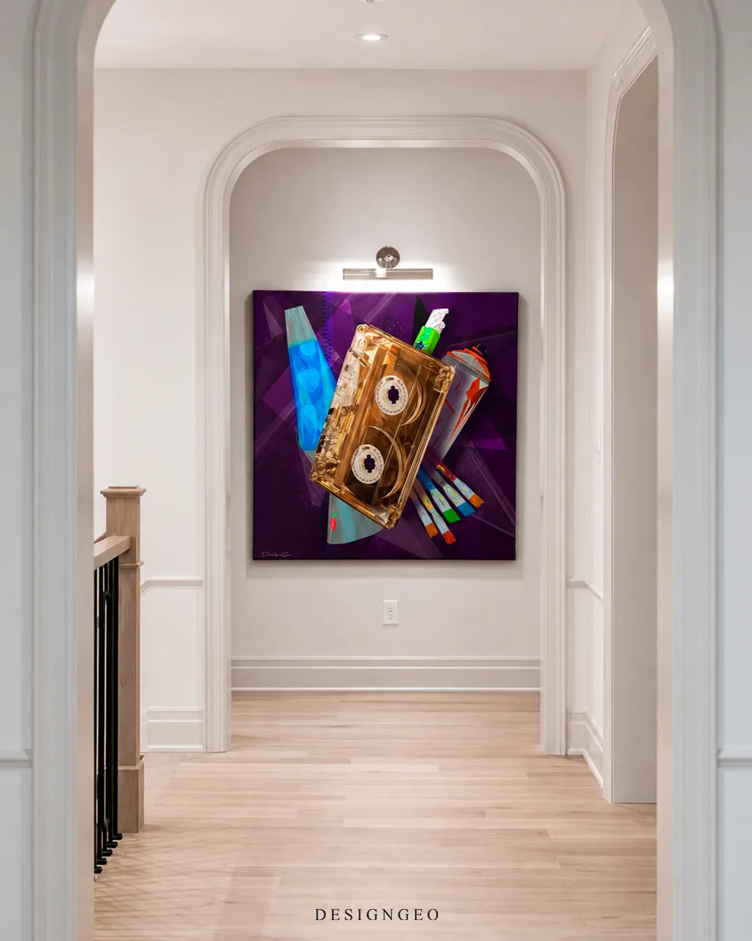Bright hallway view through an arched doorway featuring a large square retro cassette tape canvas art with a lava lamp and spray paint cans mounted on a white wall under a picture light