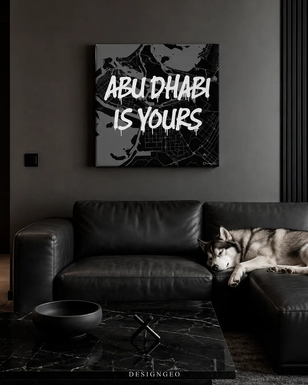 Square monochrome Abu Dhabi Is Yours canvas wall art mounted above a dark leather sectional sofa with a husky dog sleeping on it