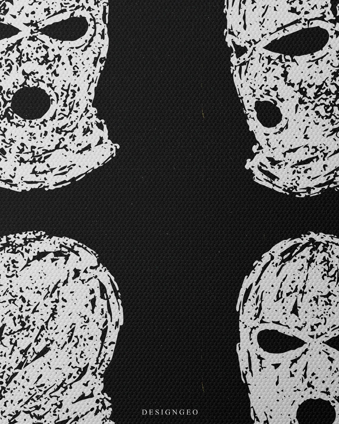 Close-up macro view showing fine canvas texture with a distressed white stencil print of a ski mask against a black canvas backdrop