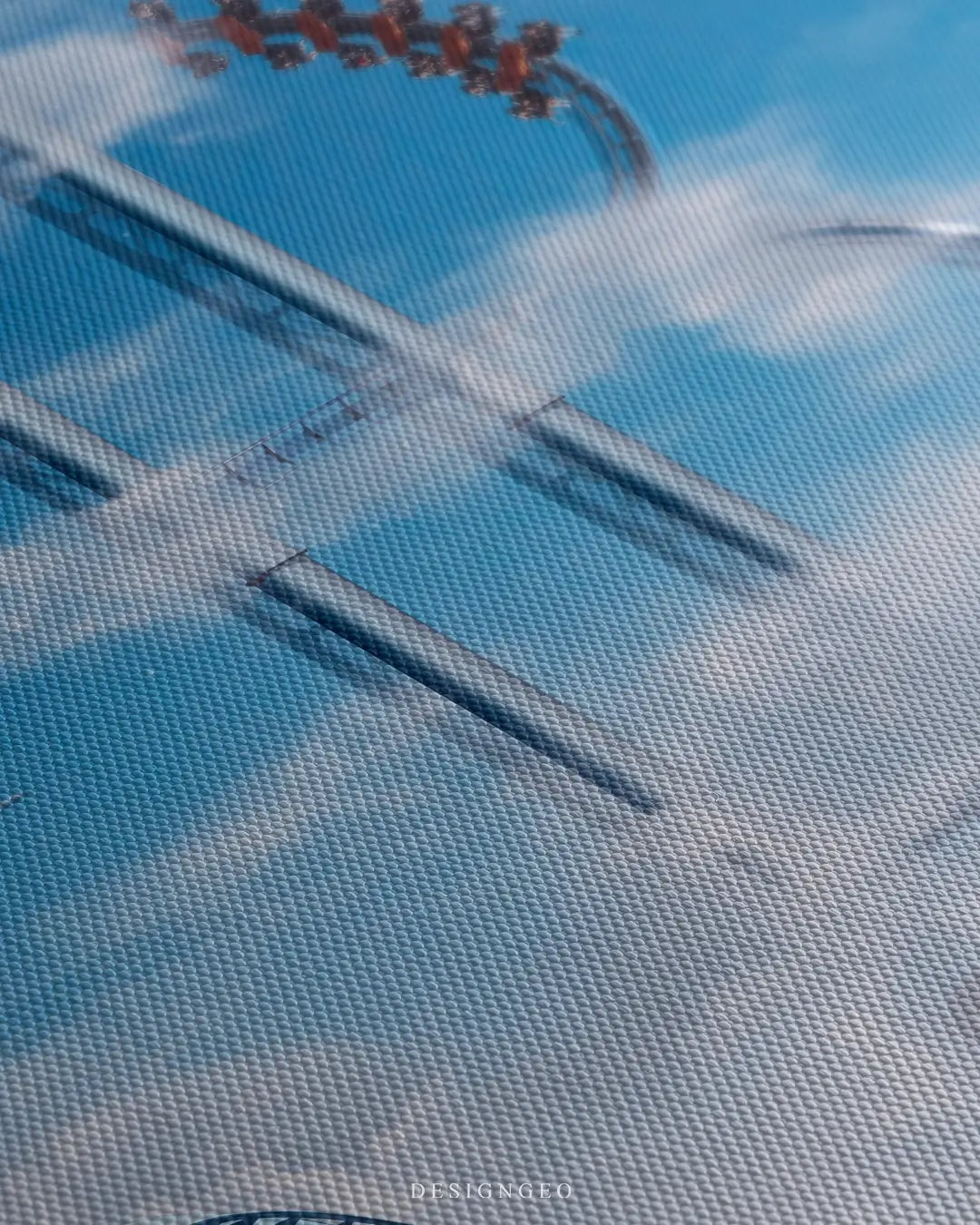 Close-up of surreal wall art featuring a roller coaster track shaped like the Bitcoin symbol against a bright blue sky with soft clouds