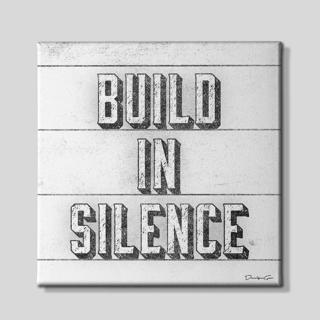 Front view of a square light gray canvas print featuring the motivational quote BUILD IN SILENCE in textured 3D block typography between thin horizontal lines