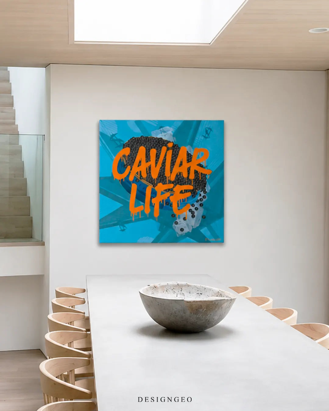Square bright blue Caviar Life pop art canvas wall art mounted on a white wall in a modern architectural dining room with a long concrete table