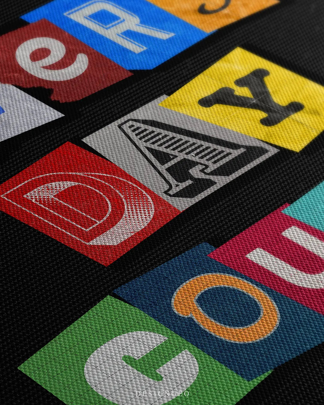 Angled close-up shot of the woven canvas grain, highlighting the sharp print quality of colorful cutout typography spelling "COUNTS" on a dark black background