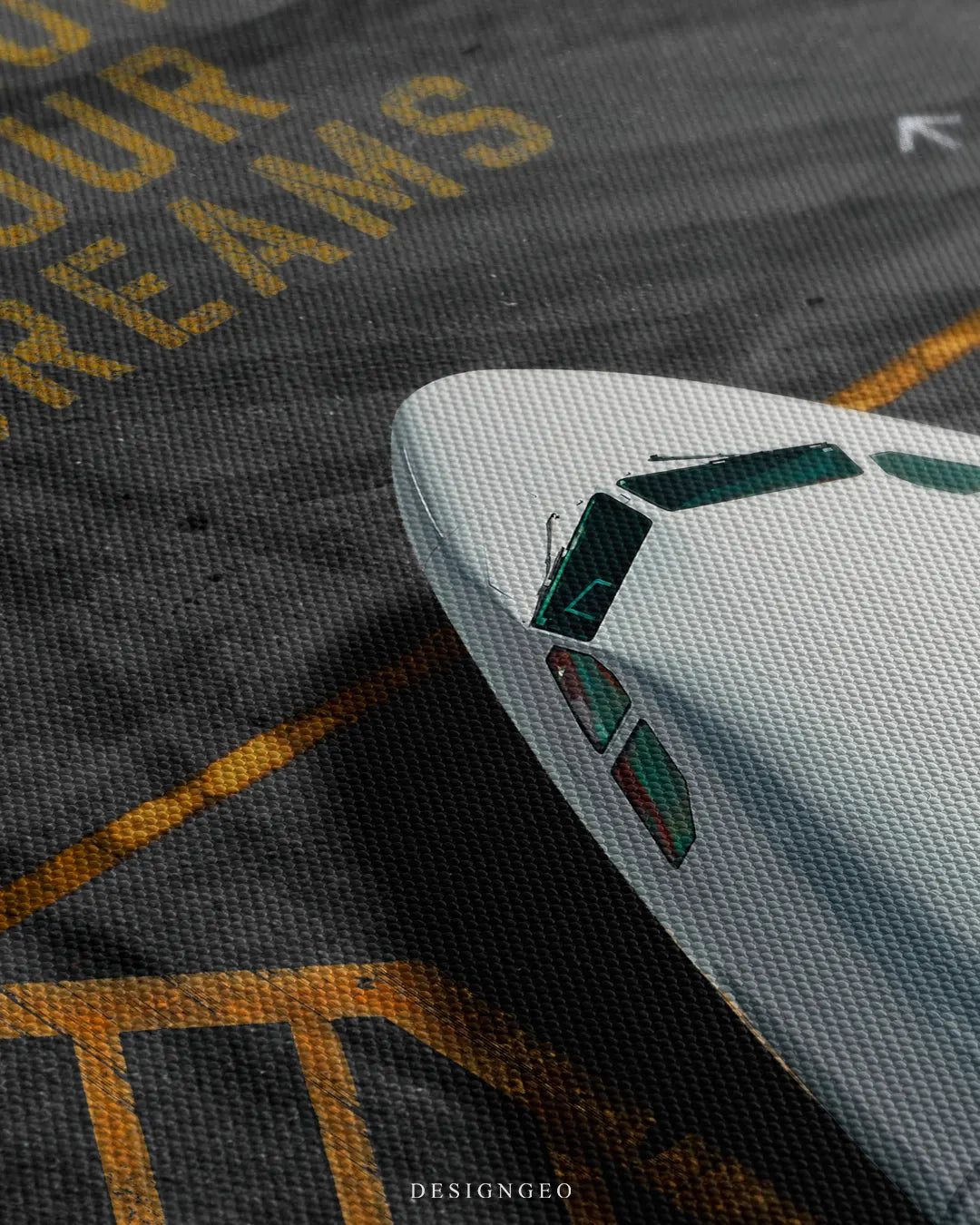 Angled close-up view of the canvas print surface, detailing the white airplane cockpit windshield and the textured yellow stencil lettering spelling "OUR DREAMS" on tarmac