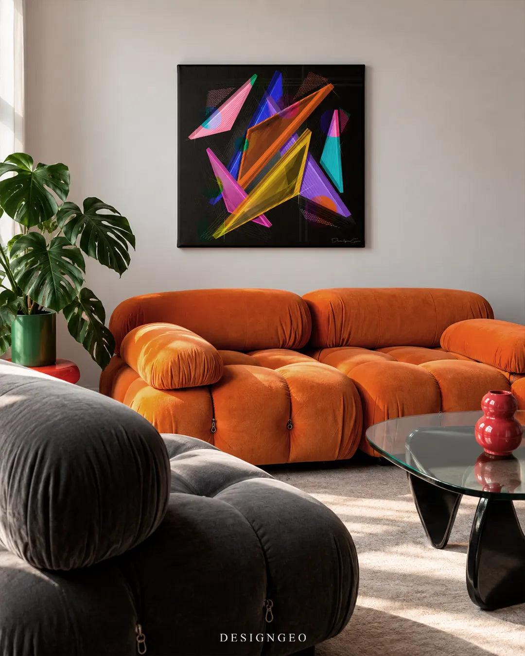 Square black canvas print featuring colorful translucent abstract geometric shapes mounted on a light gray wall in a mid-century modern living room above an orange modular velvet sofa