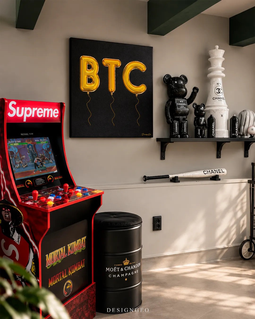 Square black canvas wall art featuring 3D shiny gold foil balloons spelling out BTC with dangling strings, mounted on a grey wall in a luxury game room next to a Supreme Mortal Kombat arcade machine and Chanel themed collectibles