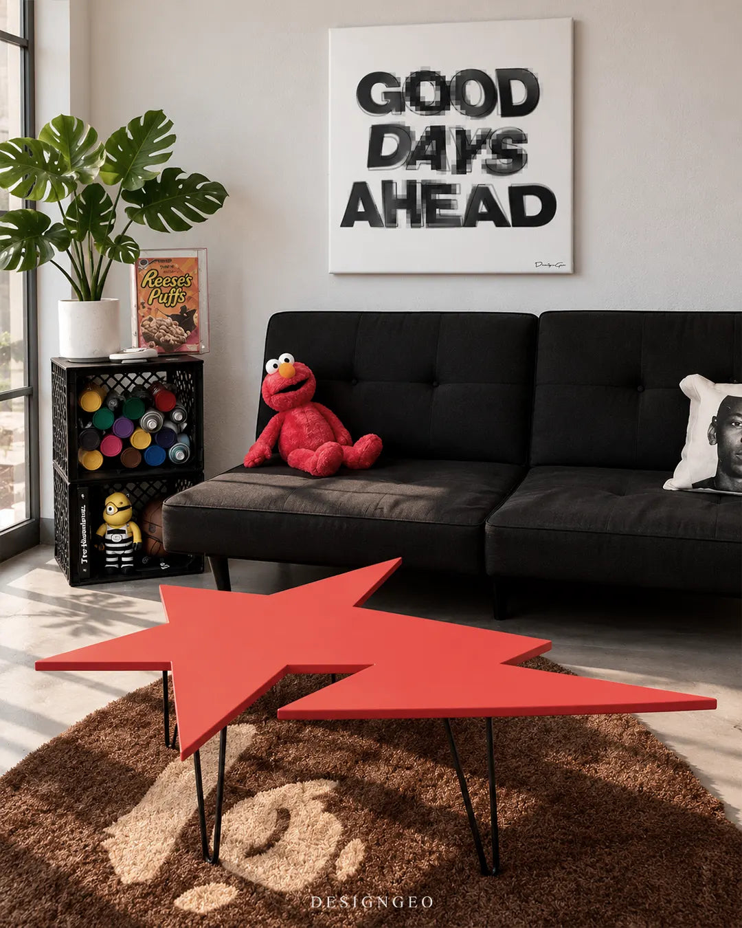 Square white canvas print featuring black motion blur typography spelling GOOD DAYS AHEAD mounted on a light wall above a black sofa with an Elmo plush toy and red star coffee table