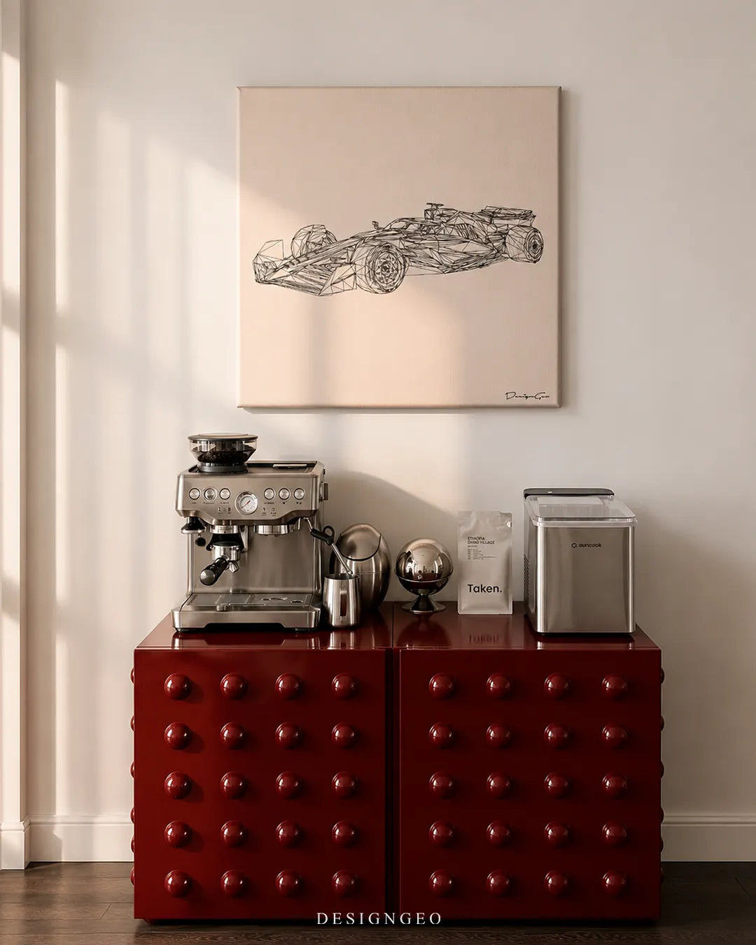 Square beige minimalist race car canvas print mounted on a white wall above a glossy deep-red studded credenza featuring a stainless steel espresso machine, specialty coffee bag, and ice maker