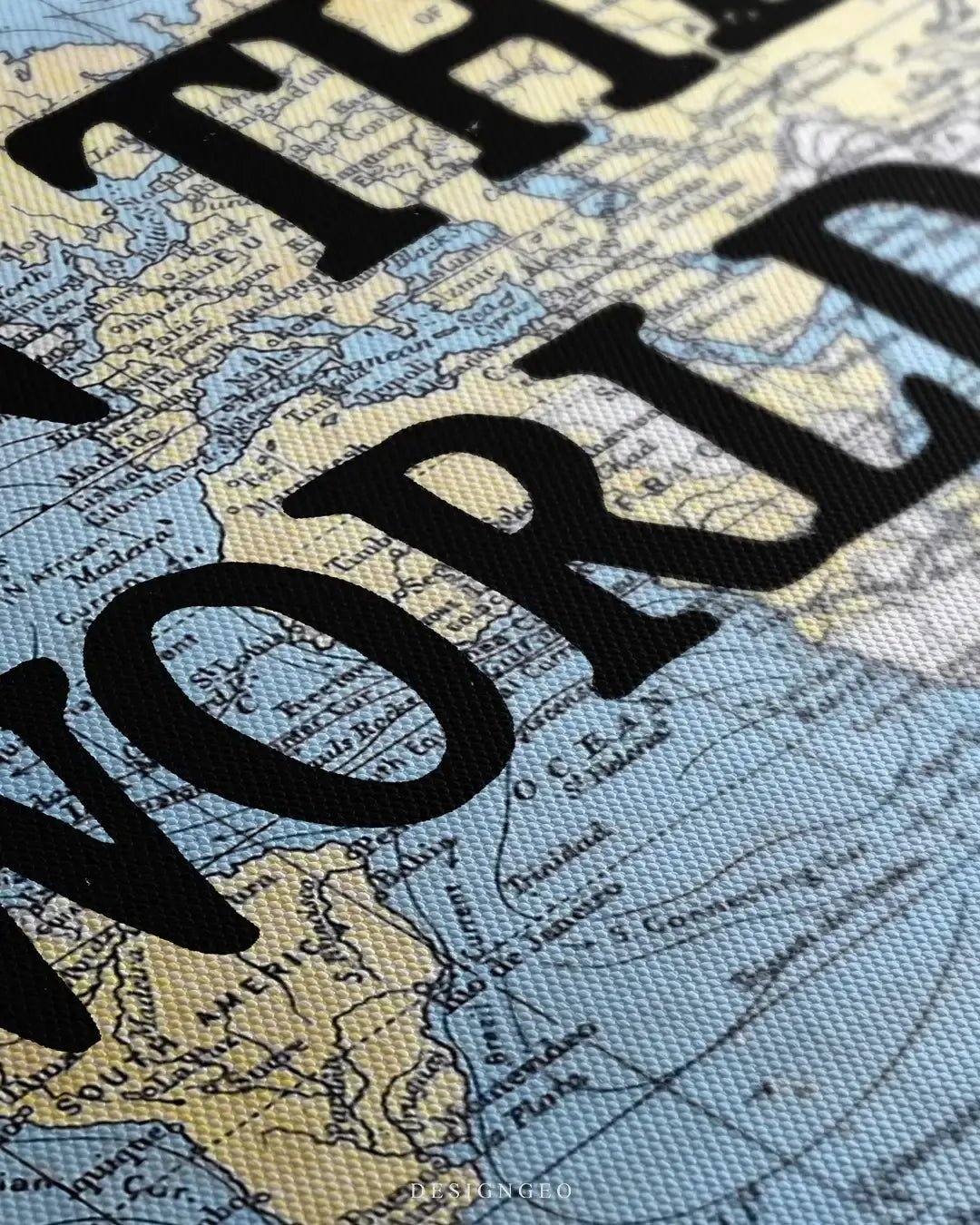 Close-up side view of a canvas wall art featuring a vintage world map with bold black typography, showing the detailed canvas texture and ink