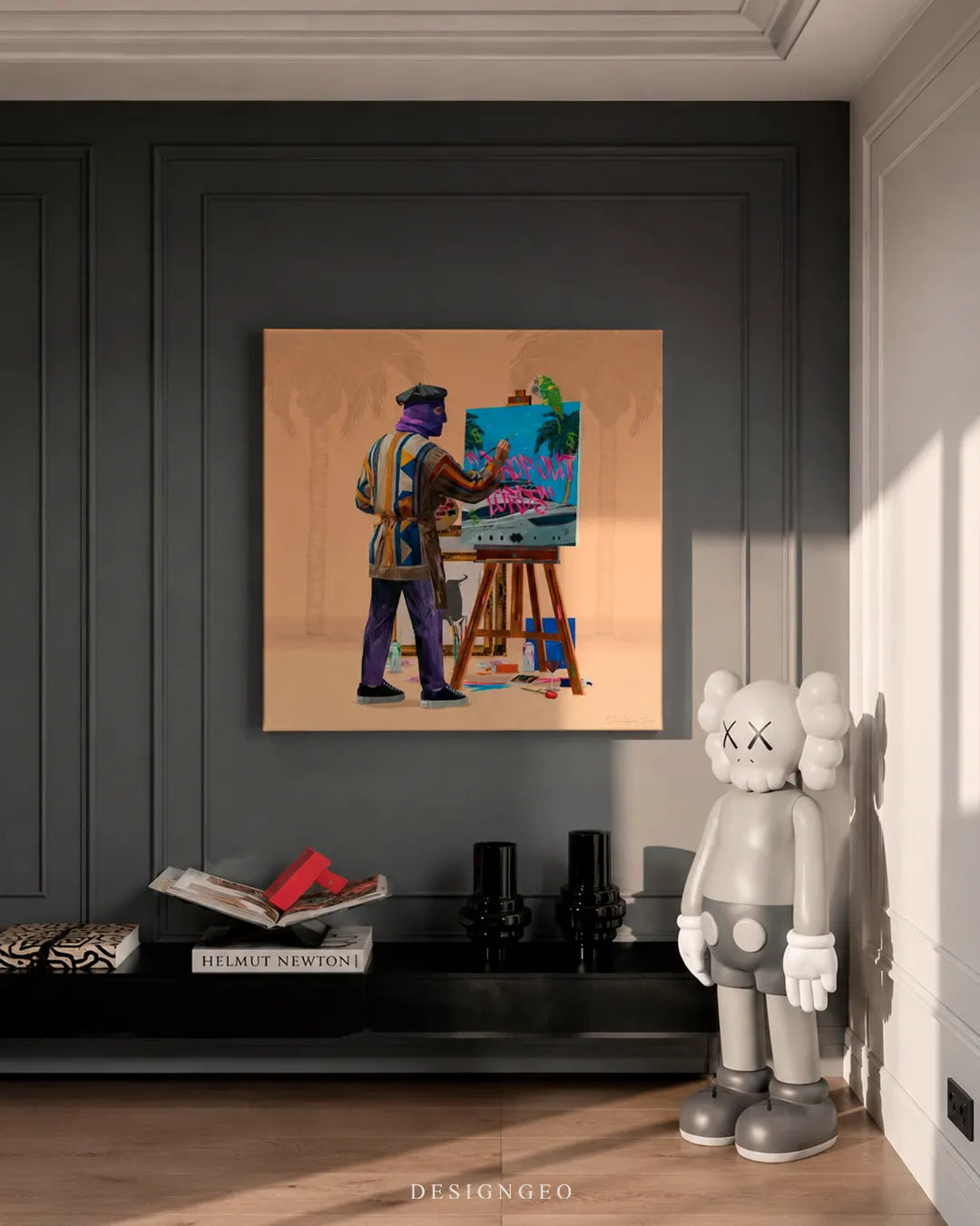 Square Painter in Marbella canvas print mounted on a dark charcoal wainscoted wall next to a white KAWS figure, black decorative vases, and a Helmut Newton art book on a console table