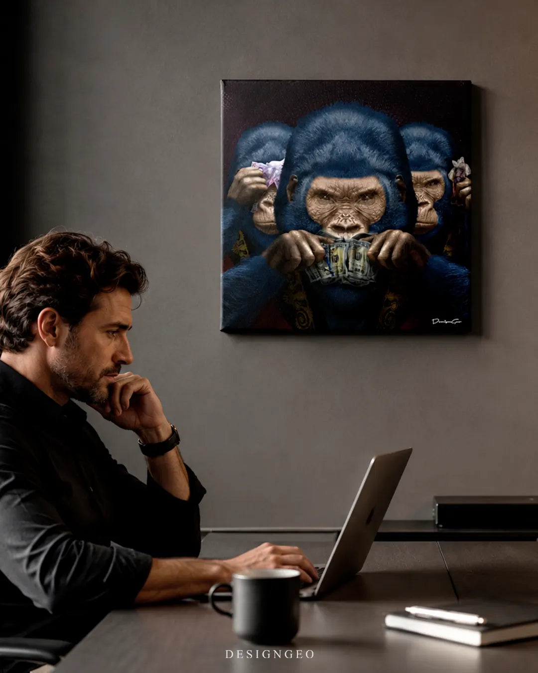 Modern office setup with a man working on a laptop below the square three wise apes canvas wall art mounted on a dark grey wall