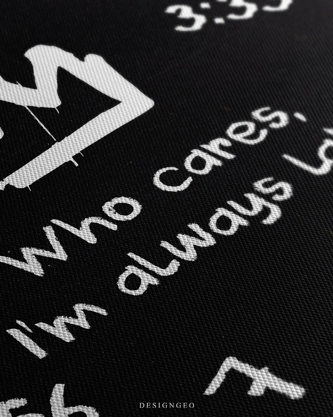 Angled extreme macro view highlighting the black woven canvas surface texture and white paint strokes forming the words Who cares, I'm always late