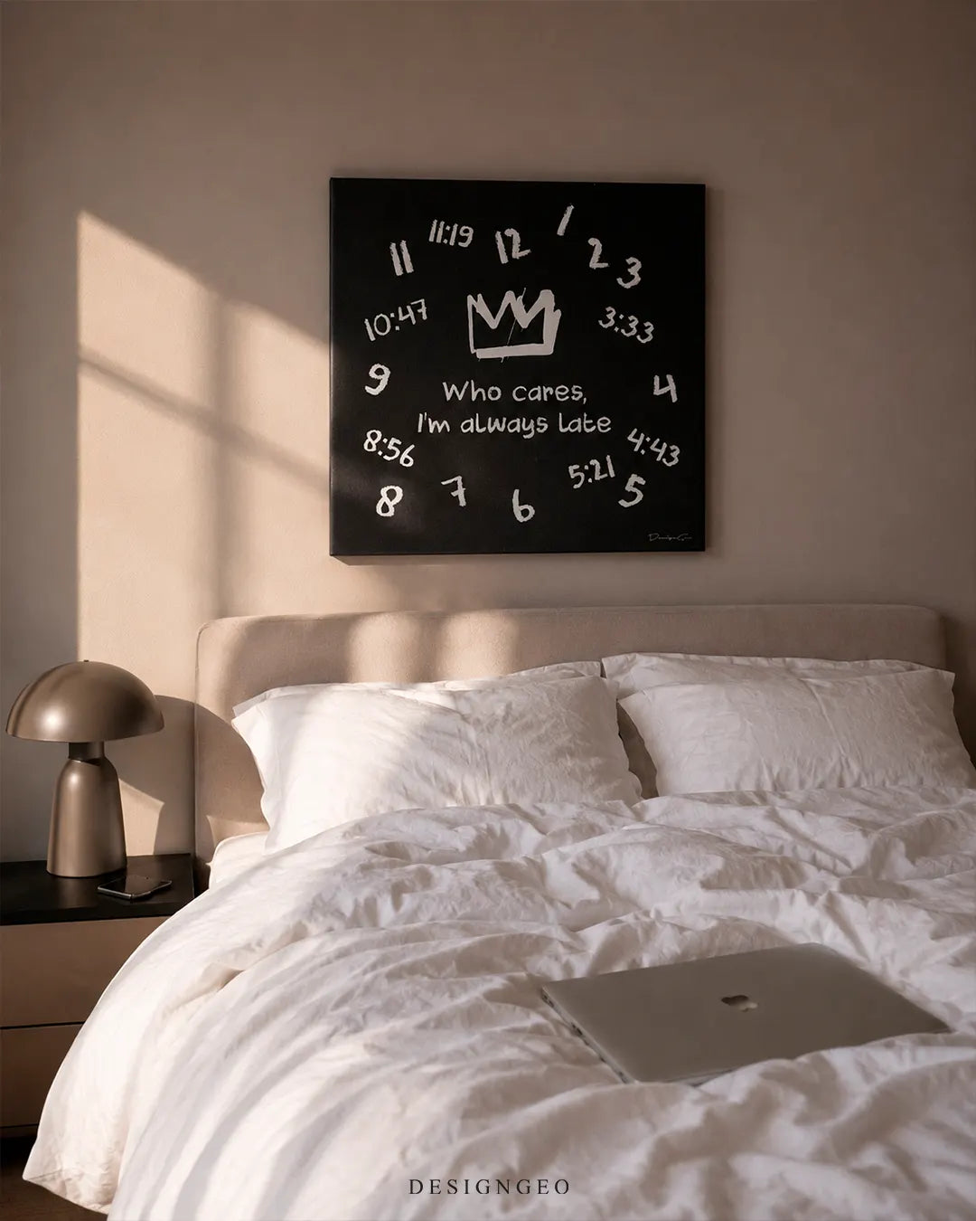 Square Who cares I'm always late black canvas wall art mounted on a beige wall above a modern bed with white linens, a nightstand lamp, and a laptop