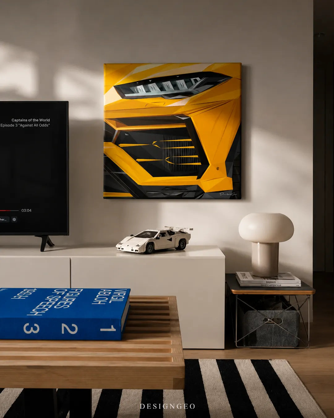 Square yellow luxury SUV canvas print mounted on a beige wall next to a TV above a white console table with a white sports car model, Virgil Abloh book, and mushroom table lamp