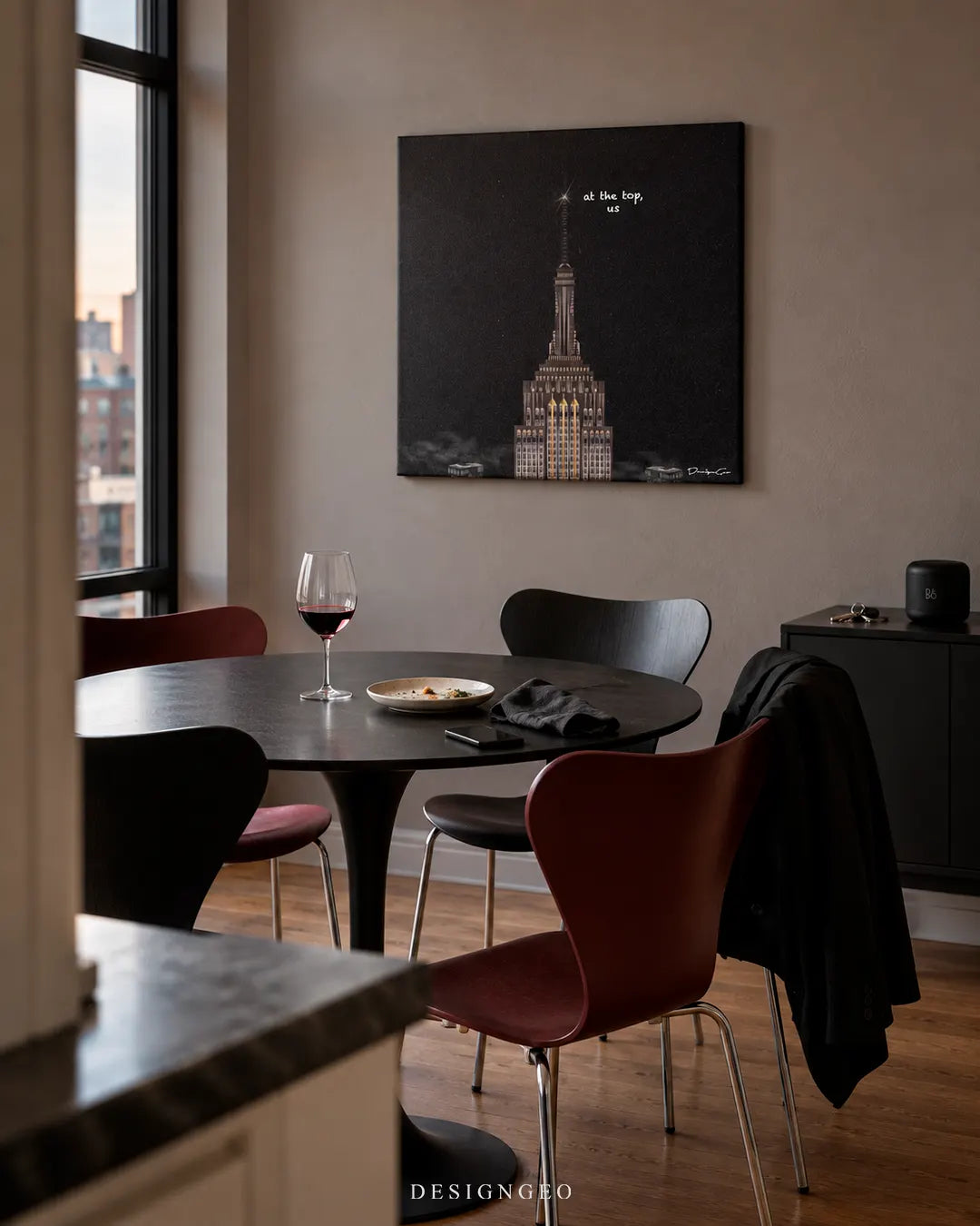 Modern luxury dining area featuring a square canvas print of the Empire State Building illuminated at night with white text reading at the top, us mounted on a warm grey wall