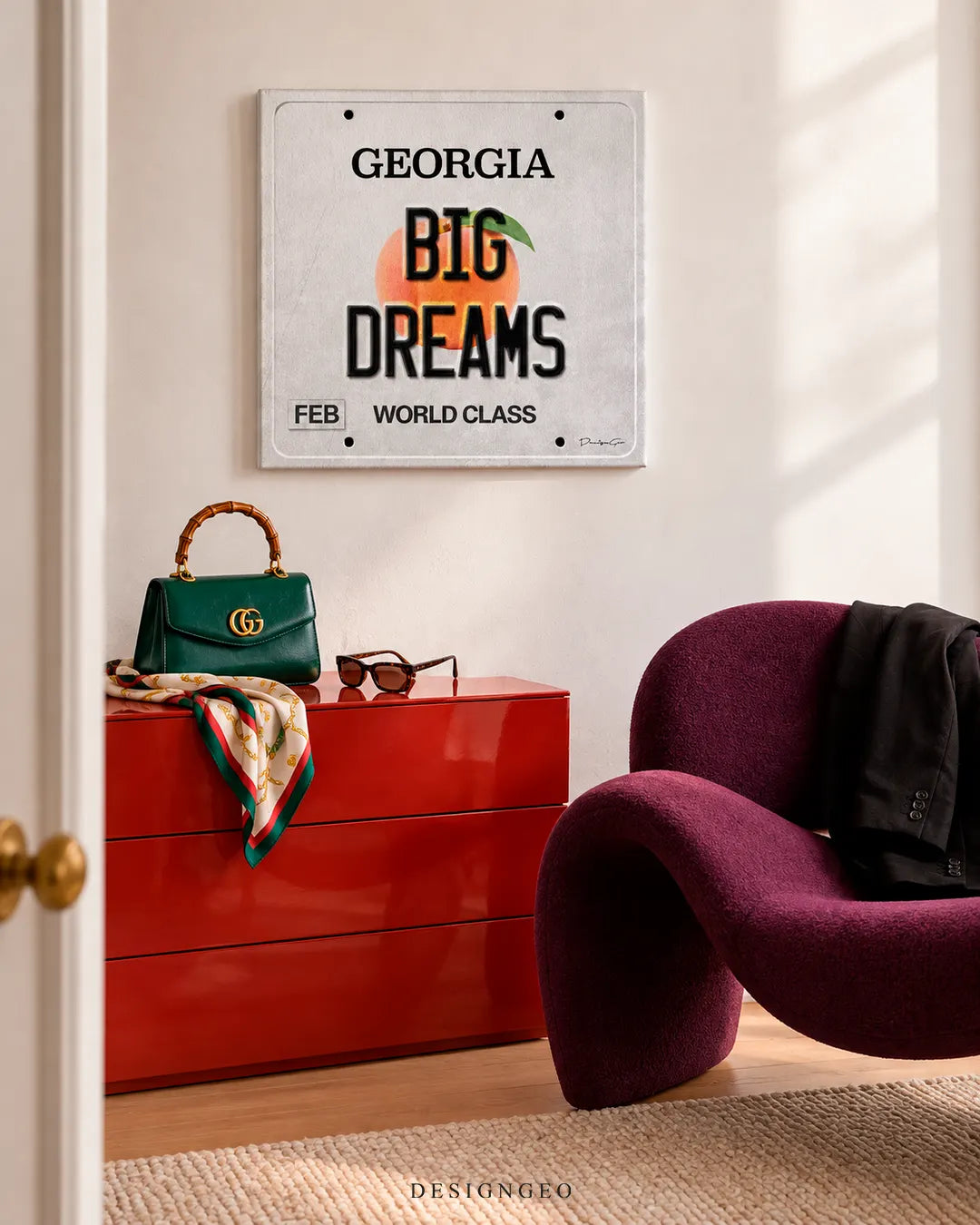 Modern luxury bedroom entry featuring a square canvas print of a Georgia license plate with BIG DREAMS text mounted above a glossy red dresser and purple lounge chair