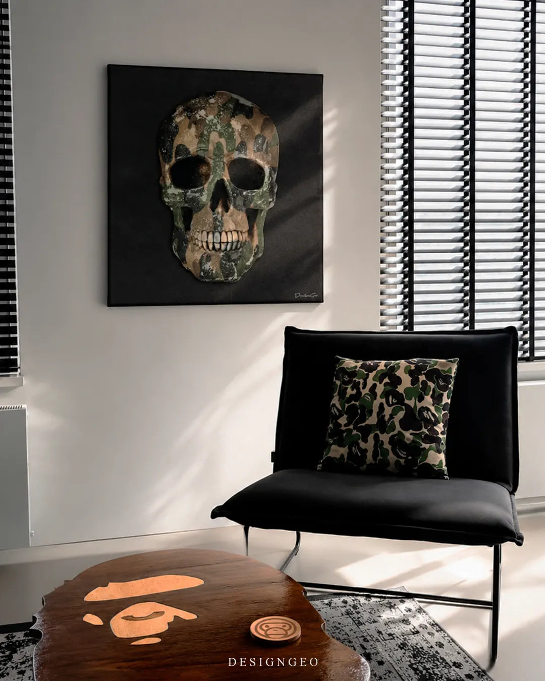 Square black camouflage skull canvas print mounted on a white wall in a modern lounge beside black venetian blinds, a black accent chair with a camo pillow, and a BAPE ape head shaped wooden coffee table