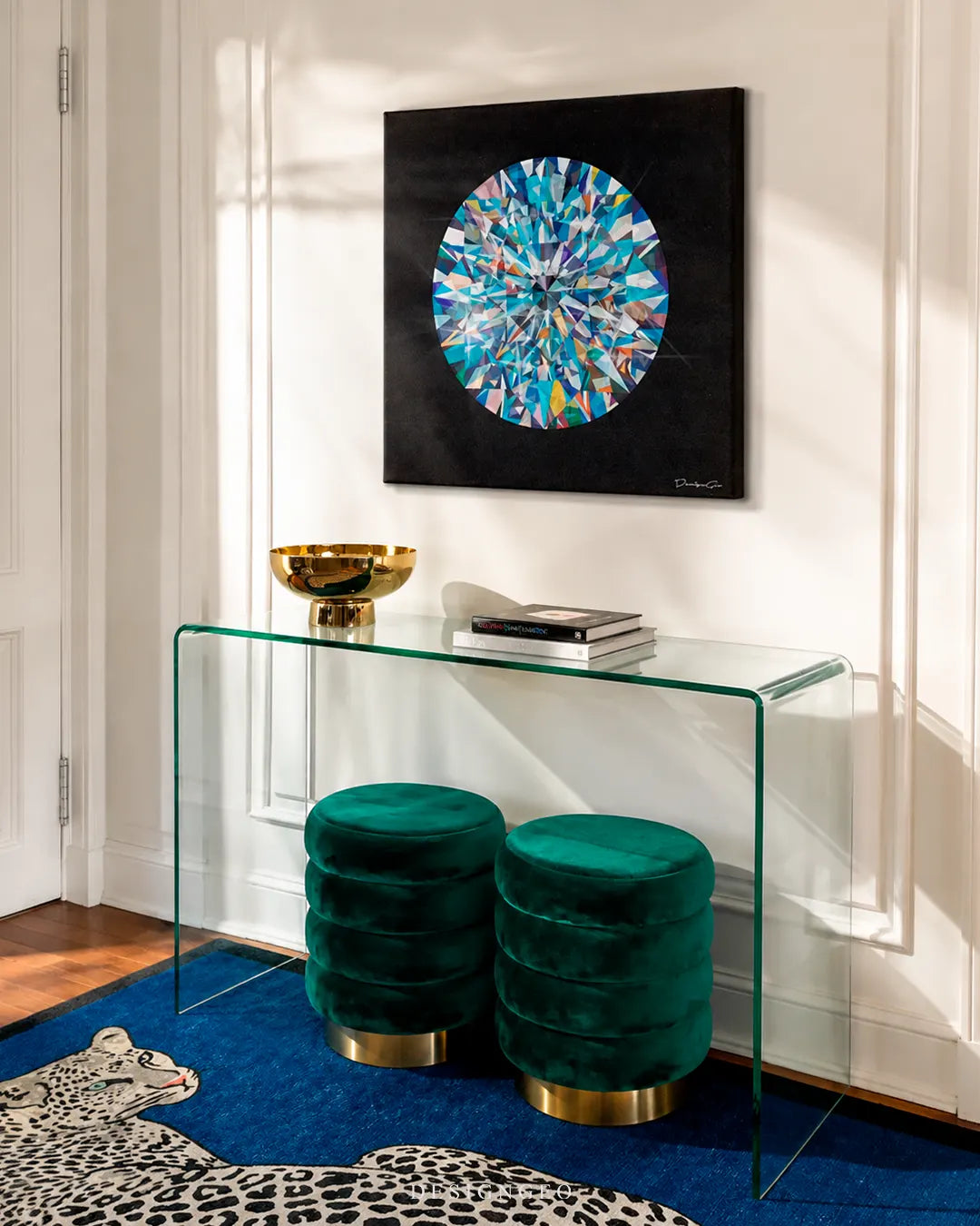 Square black diamond canvas print displayed on a white wall above a clear glass console table and green velvet ottomans in a modern luxury entryway