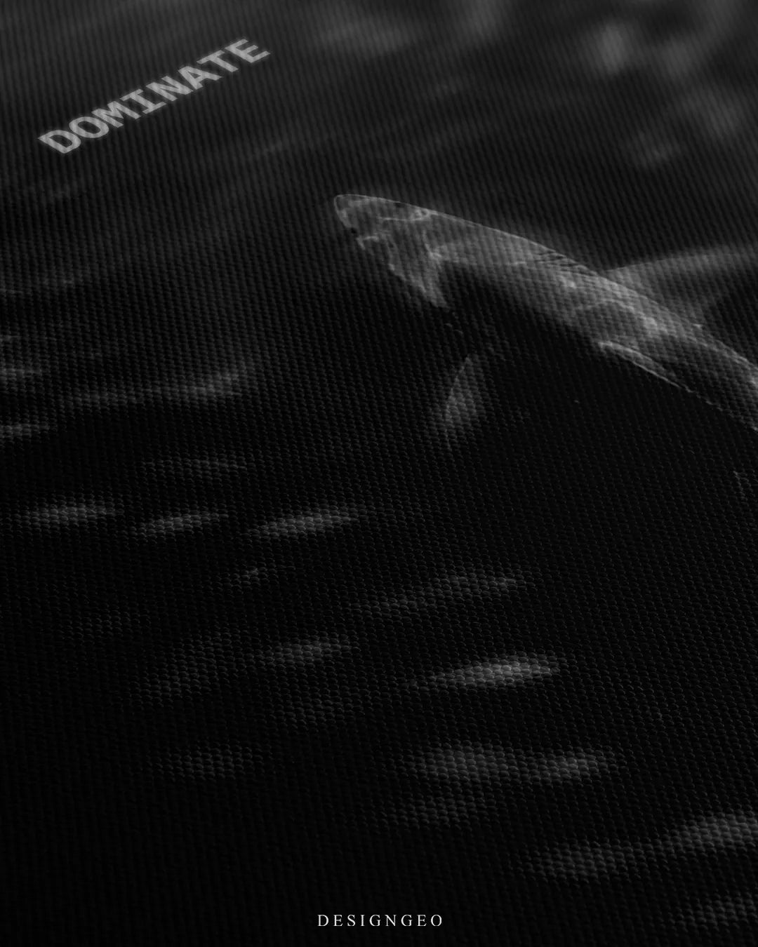 Angled detailed macro texture of black woven canvas print showing top down view of a shark swimming upward with Dominate quote