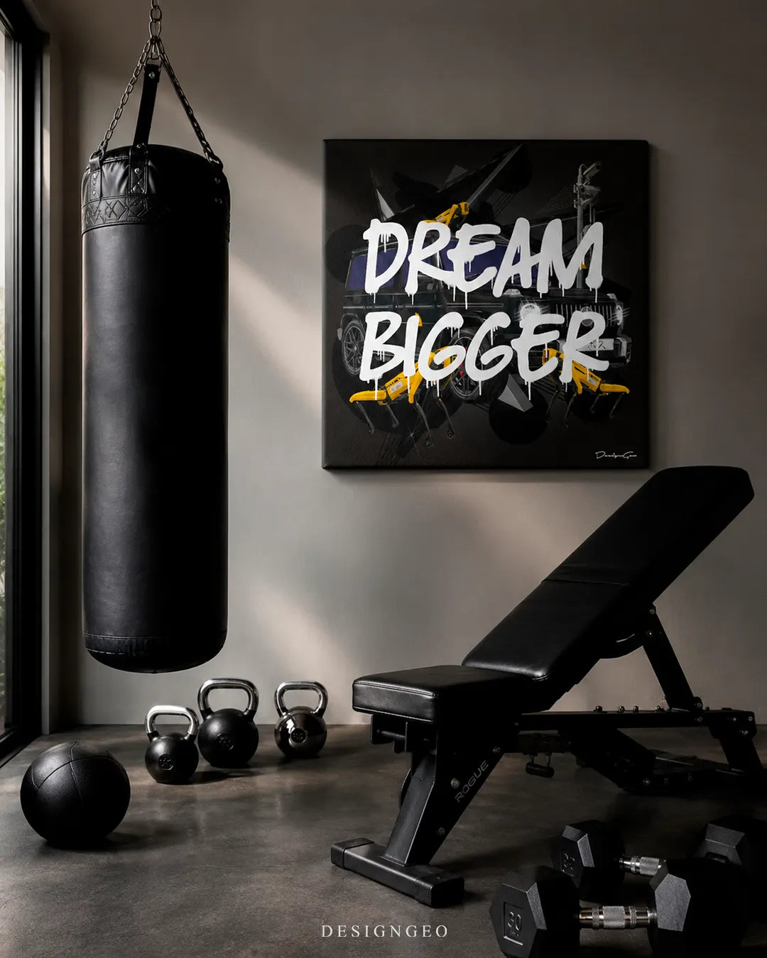 Square dark grey Dream Bigger canvas print mounted on a grey wall in a luxury home gym next to a black heavy punching bag, kettlebells, and Rogue workout bench