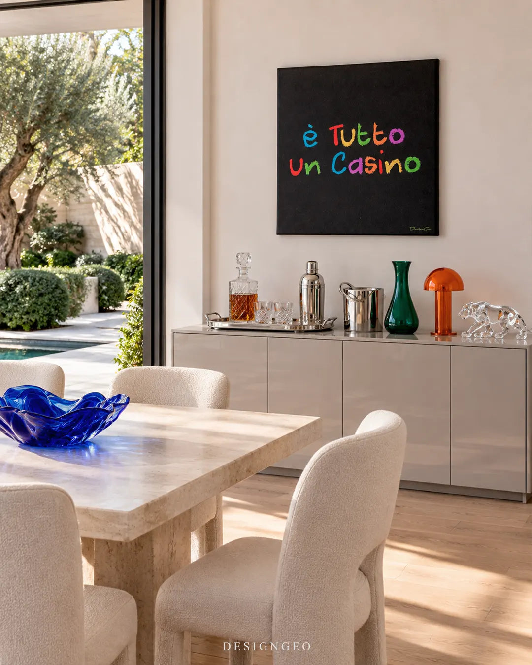 Square black canvas print featuring colorful handwritten E TUTTO UN CASINO Italian quote typography mounted on a beige wall in a modern dining room above a grey bar cabinet