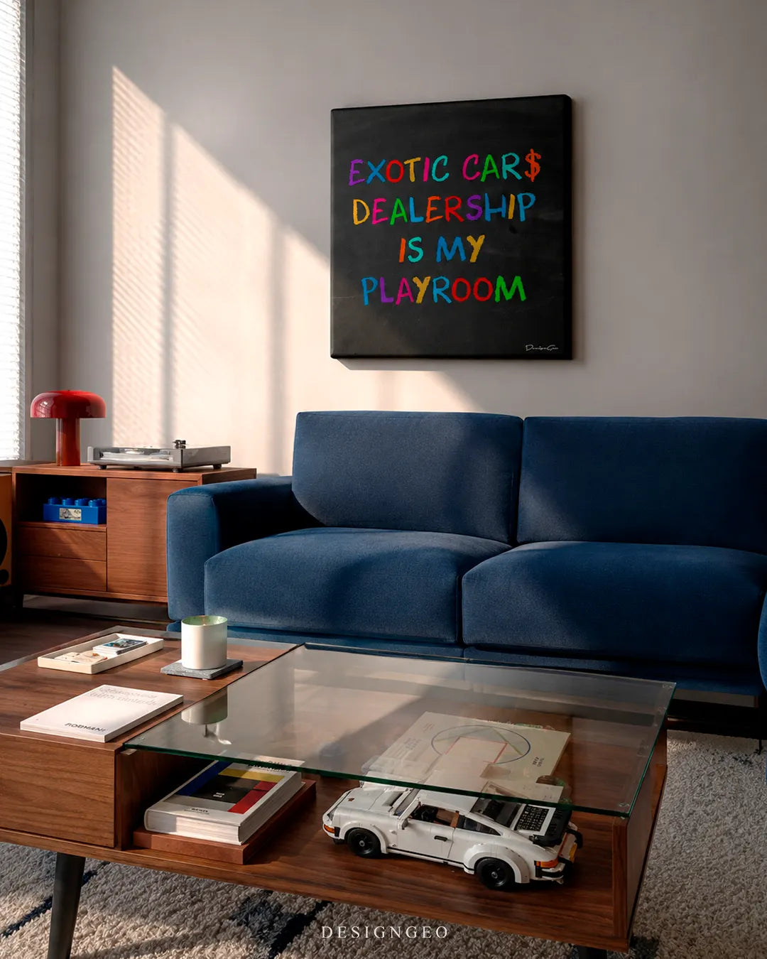 Square Exotic Cars Dealership canvas print mounted on a light grey wall above a royal blue velvet sofa, wooden coffee table with a white Porsche model car, and red desk lamp