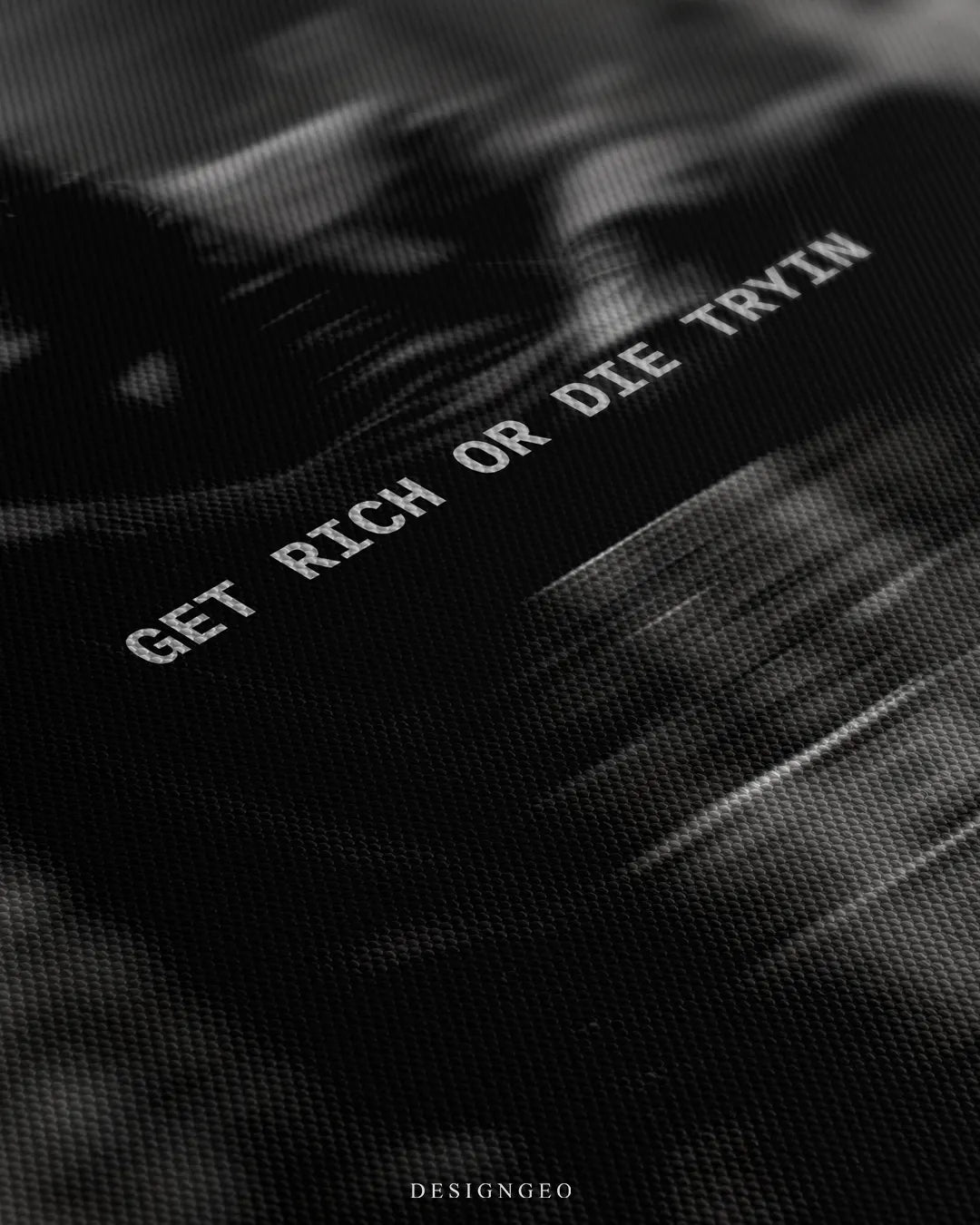 Angled detailed macro texture of black woven canvas print showing man sitting on money stacks in a bank vault with Get Rich Or Die Tryin quote