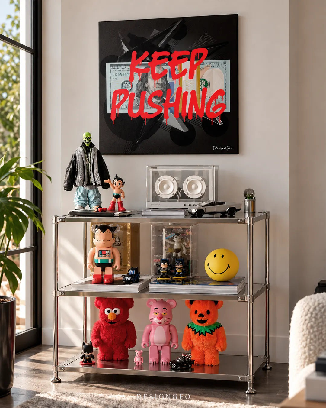 Keep Pushing red graffiti text over one hundred dollar bill square canvas wall art displayed on a white wall in a modern collector room above a chrome shelving unit filled with art toys and collectibles