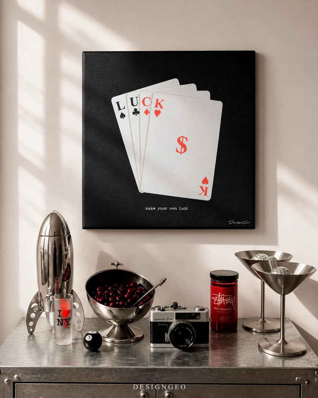 Modern interior desk setup displaying a square black canvas print featuring four playing cards spelling LUCK with a red dollar sign and the text make your own luck at the bottom