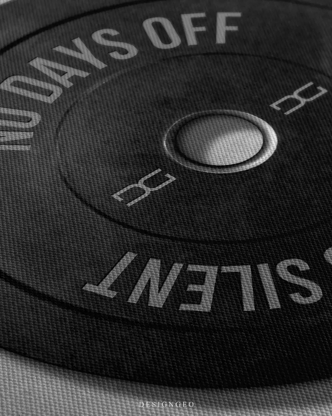 Close-up on a rugged black barbell plate canvas print with the motivational gym quote "No Days Off Strength is Silent" in bold white lettering against a minimalist grey and white background