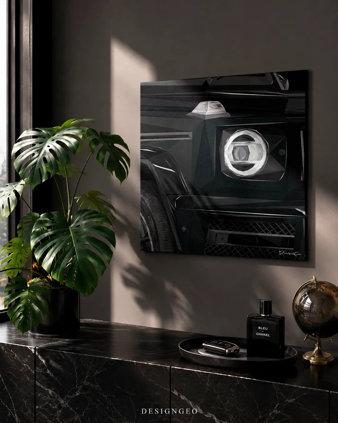 Square black SUV canvas print mounted above a dark marble credenza with a Monstera plant, Bleu de Chanel perfume bottle, and a bronze globe