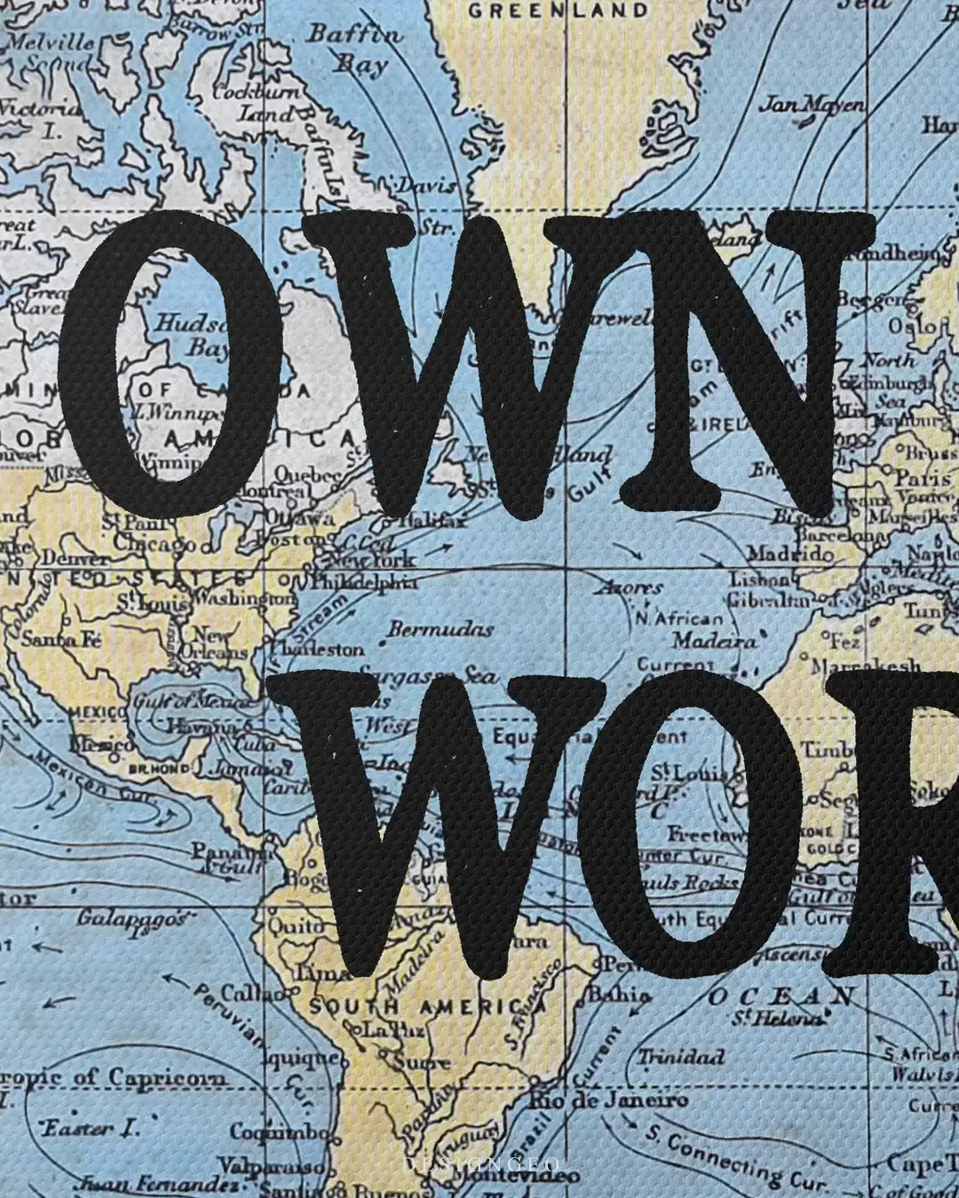 Macro shot of a world map canvas print with the motivational phrase OWN THE WORLD in serif font over a detailed antique-style ocean and continent background