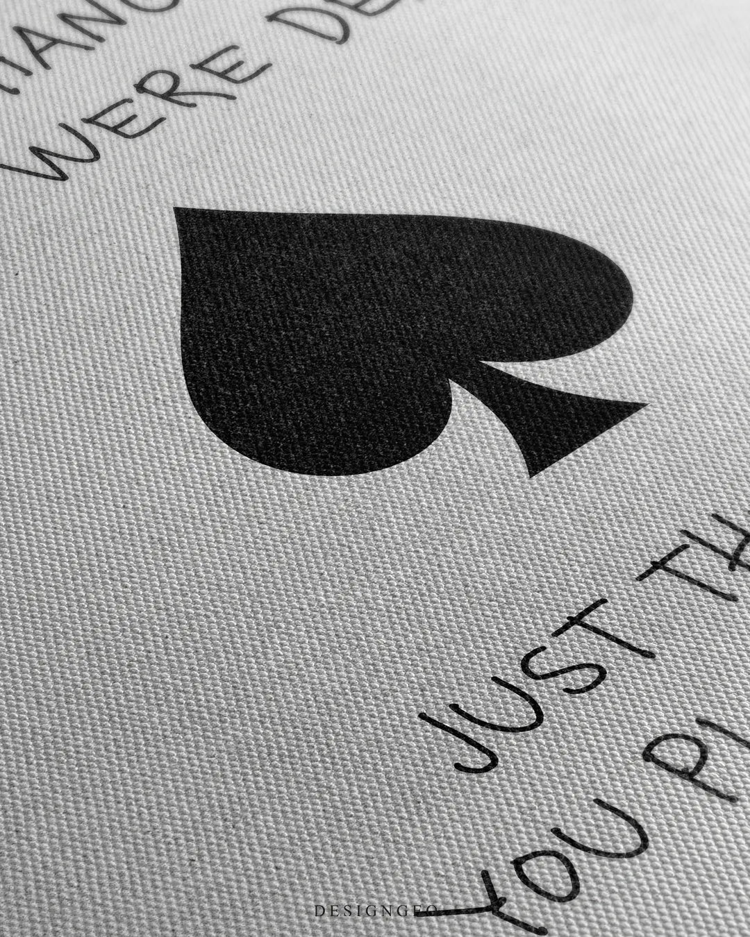 Angled macro view detailing fine woven canvas fabric grain, crisp black ink printing of the playing card quote, and central spade symbol design