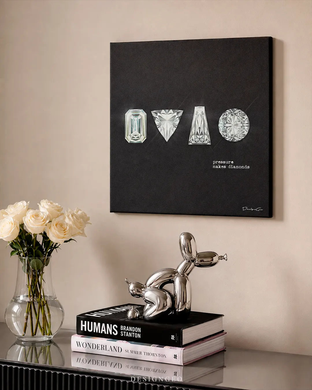 Square Pressure Makes Diamonds canvas print mounted on a beige wall above a glass console table with a silver balloon dog sculpture, white roses in a glass vase, and coffee table books