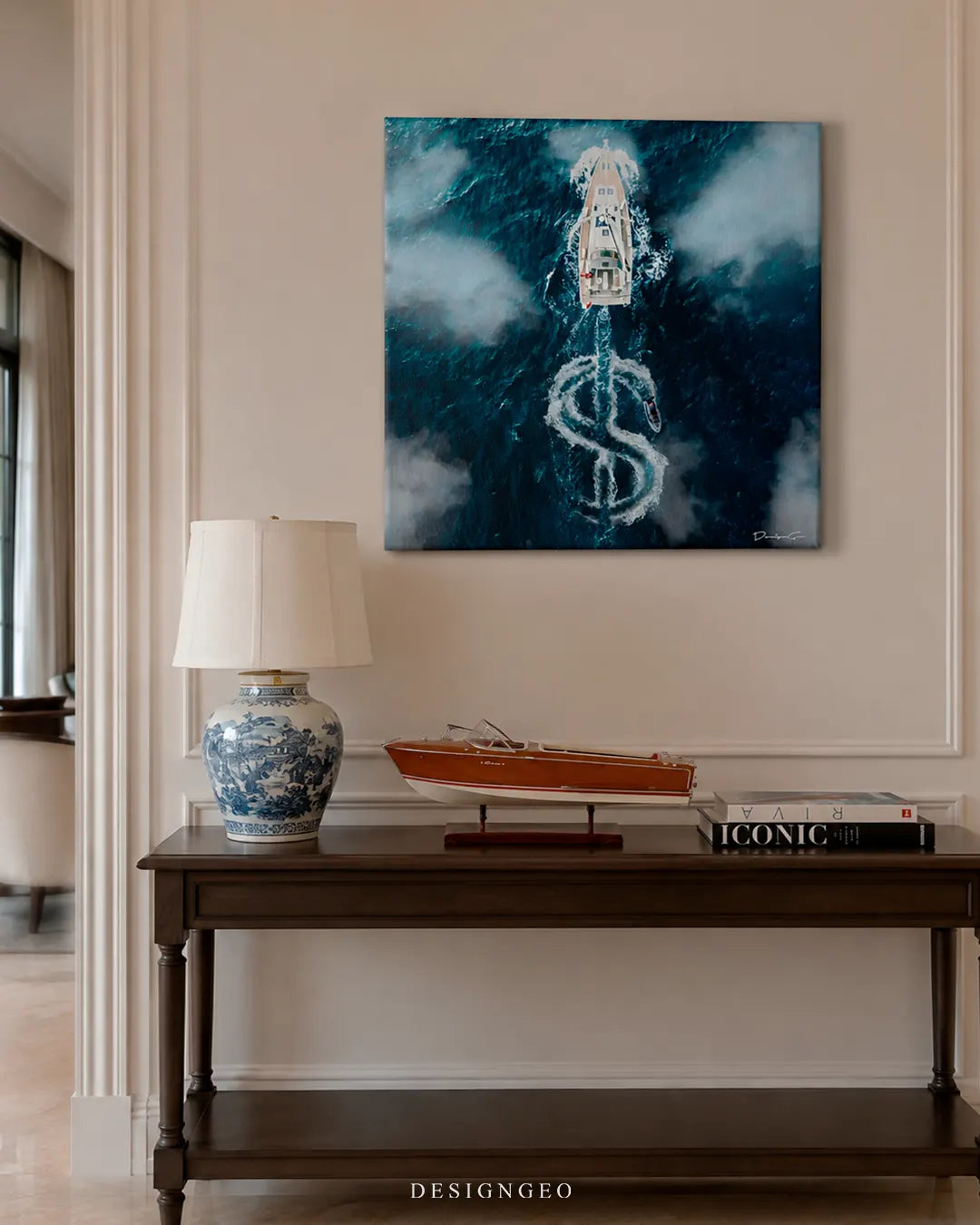 Square Summer Spirit yacht canvas print mounted on a beige wall above a dark wood console table with a blue porcelain lamp, Riva coffee table book, and miniature wooden speedboat model